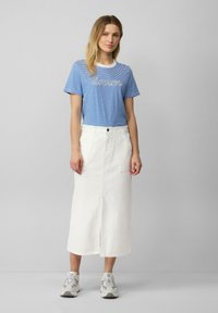 T-shirt a righe blu con testo "dream", abbinato a una gonna di jeans bianca con tasche anteriori e uno spacco centrale. Sneakers grigie chiare completano il look.