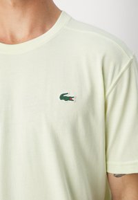 Lys gul bomulds t-shirt med rund hals og korte ærmer, der har et lille grønt krokodille-logo på brystet.