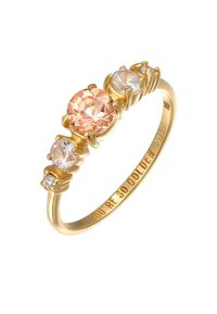 Guldpläterad ring med en central ljusrosa ädelsten, omgiven av två mindre klara stenar, med graverad text på insidan av bandet.