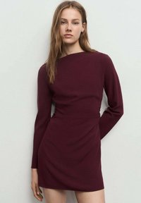 Vestido burdeos de manga larga con silueta ajustada y detalle fruncido en la cintura, confeccionado en una tela suave, de largo hasta la rodilla, diseño minimalista.