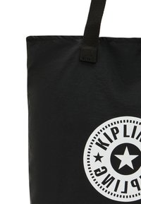 Borsa a tracolla nera realizzata in materiale leggero, caratterizzata da un grande logo circolare bianco con testo e dettagli a stella. Spallacci in tessuto robusto.