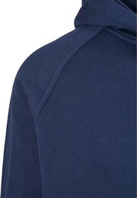 Gros plan de l'épaule et du haut du dos d'un sweat à capuche bleu marine avec des coutures visibles et une texture de tissu.