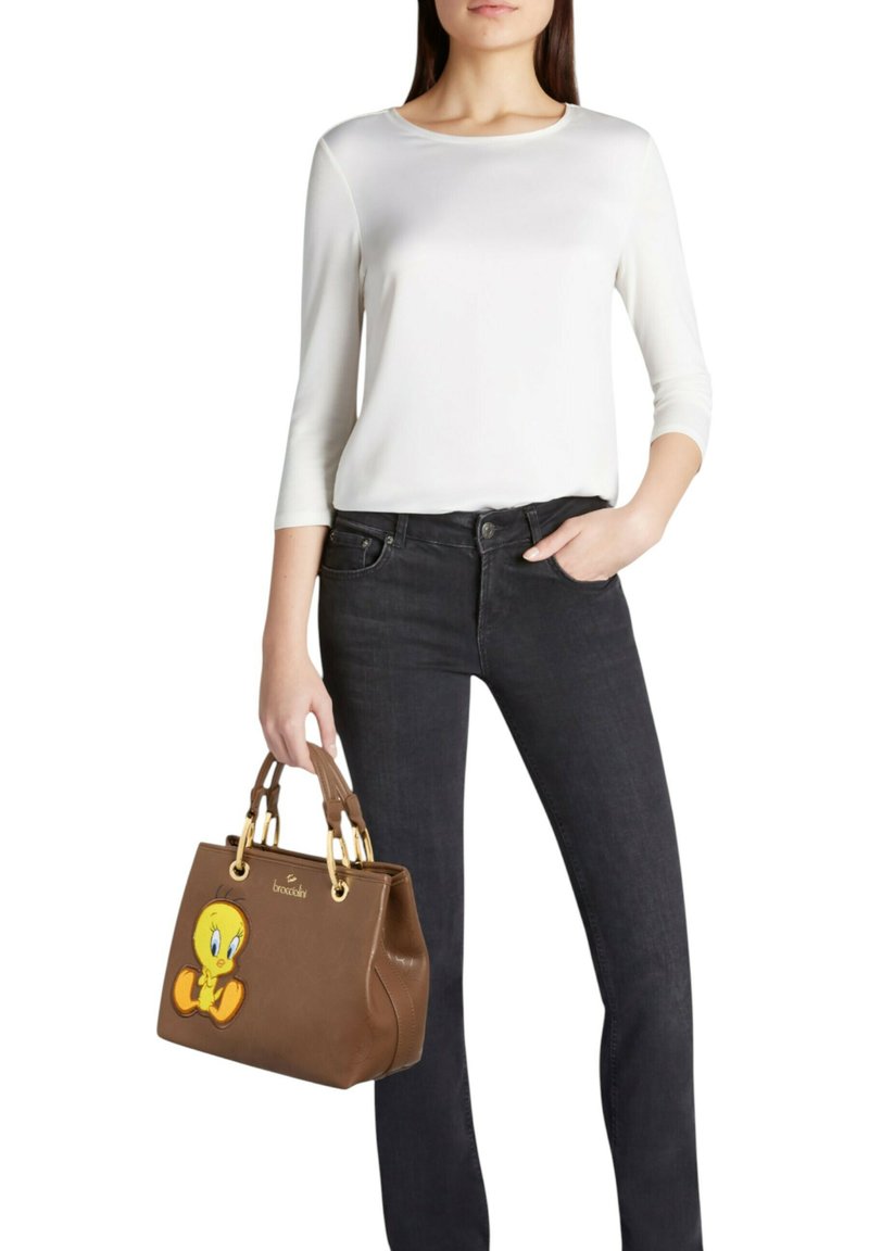 Borsa marrone con design cucito di Tweety Bird, finiture dorate e due manici, abbinata a una maglietta bianca e jeans neri.