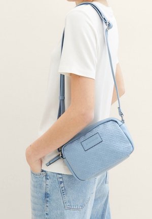 Light blue crossbody bag with woven pattern, rectangular shape, adjustable strap, and branded tag. Smooth texture and minimalist design.
