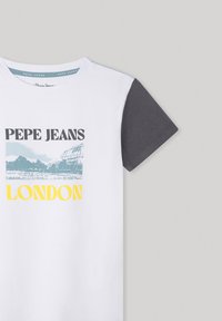 Camiseta blanca con texto negro "PEPE JEANS", gráfico azul de una escena londinense, texto amarillo "LONDON" y una manga gris oscuro.