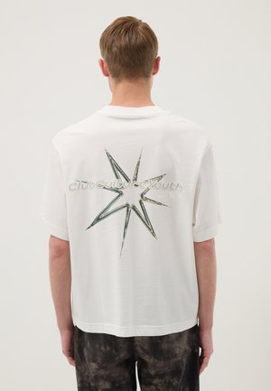 Joven de espaldas que lleva una camiseta blanca con una gran estrella estilizada y un diseño de texto en la parte trasera.