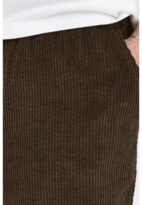 Brown corduroy fabric with vertical ribbed texture. Features a straight cut and side pockets. Background shows a white top just above the waistband.