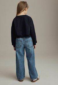 Sweatshirt noir court avec ourlet côtelé associé à un jean léger bleu clair à coupe ample. Les jeans possèdent de grandes poches arrière et des ourlets retroussé.