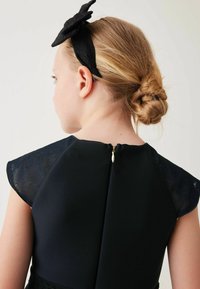 Schwarzes Kleid mit transparenten Kurzärmeln und strukturiertem Oberteil, mit einem Reißverschluss auf der Rückseite und einem Stoffbogen-Haarband in Schwarz.