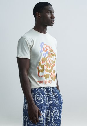 Krēmkrāsas t-krekls ar daudzkrāsainu grafisko apdruku. Komplektā ar zilām rakstainām biksēm ar baltām ilustrācijām. Gluda tekstūra.