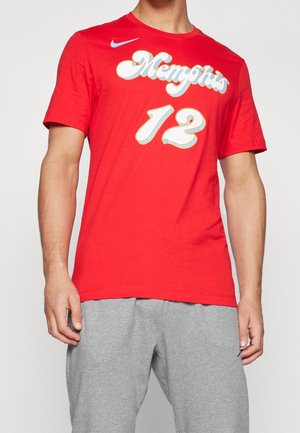 Man draagt een rood T-shirt met korte mouwen met de tekst "Memphis 12" en een Nike-logo, gecombineerd met lichtgrijze joggingbroek tegen een effen achtergrond.