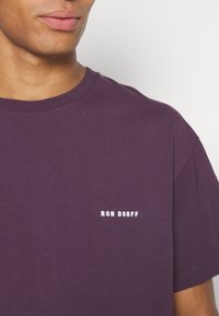 Purple cotton t-shirt with a crew neckline and short sleeves. Features a white text logo "RON DORFF" on the left chest area.