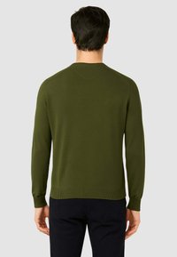Maglione lavorato a maglia di colore verde scuro con maniche lunghe, collo rotondo e polsini e orlo a costine. Tessuto liscio, design aderente e branding minimale.