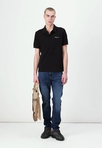 Tricou polo din bumbac negru, cu mâneci scurte, având un mic logo pe piept. Purtați cu blugi din denim albastri și cu o geantă bej.