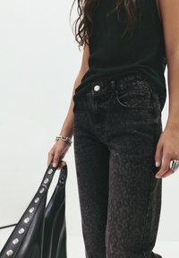 Črne jeans hlače izdenimu z diskretno leopardjim vzorcem, ki imajo pet žepov in srebrn gumb. Črna usnjena torbica z metalnimi detajli je v roki.