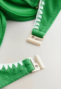 Groene textuurstof met witte stiksels, voorzien van metalen sluitingen in een rechthoekige vorm voor een veilige sluiting.