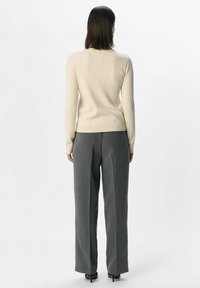 Beige ribbat tröja med en figurn�ära silhuett. Matchad med grå högmidjade byxor. Materialet verkar mjukt; subtil texturdetalj synlig.