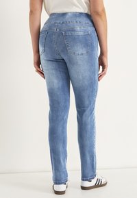 Ljusblå denimjeans med en slät struktur, figurnära design och två bakfickor. Bärs med en vit skjorta och sneakers.