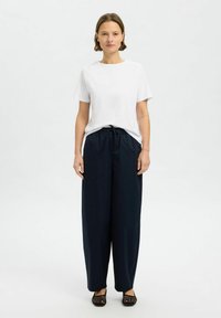 Bílý tričko s krátkým rukávem v kombinaci s námořnickými širokými kalhotami s elastickým pasem, doplněné o černé tkané slip-on boty.