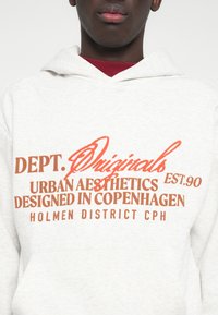 Sweatshirt cinza claro com texto laranja em destaque que diz "DEPT. Originals EST. 90 Urban Aesthetics Designed in Copenhagen Holmen District CPH."