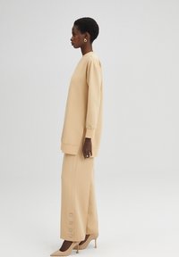 Beige oversize mikina s dlhými rukávmi, skombinovaná s širokými nohavicami so zarážkami na leme. Hladká textúra.