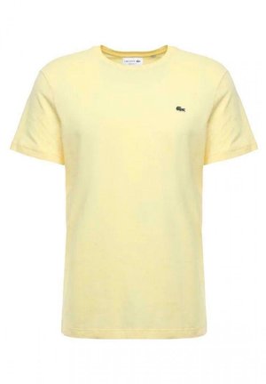 Żółta bawełniana koszulka z krótkimi rękawami, okrągłym dekoltem i małym zielonym haftowanym logo po lewej stronie klatki piersiowej.