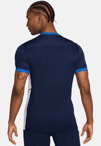 Maglietta sportiva navy con accenti blu, maniche corte, tessuto a rete e design con pannelli laterali. Presenta un collo a rotondo e una forma aderente.