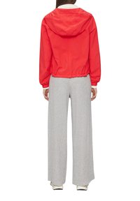 Raudona lengva striukė su gobtuvu, elastinėmis rankovėmis ir liemeniu. Derinama su pilkomis plačiomis kelnėmis, turinčiomis tekstūruotą raštą.