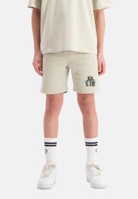 Beige katoenen shorts met een elastische tailleband, voorzien van een grafische print van een olifant en turquoise accenten. In combinatie met witte sneakers en gestreepte sokken.