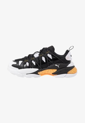 Zapatilla deportiva en blanco y negro con entresuela salpicada de naranja, parte superior de malla y sintética, diseño con cordones y logo de Puma en el lateral.