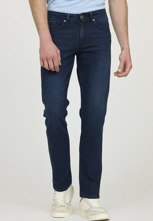 Jean foncé en denim à coupe slim. Présente un design classique à cinq poches et une fermeture par bouton métallique. Associé à des baskets claires.