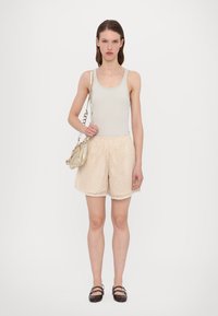 Lichtgrijze tanktop gecombineerd met crèmekleurige wafelkatoenen shorts. Het model houdt een beige handtas vast met een metalen kettingriem en draagt donkere flats.