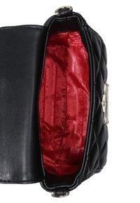 Svart läderhandväska med kviltad utsida, öppen som avslöjar en röd satininteriör och en låsdetalj.