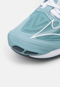 Ljusblå atletisk sko med en texturerad ovandel, vita detaljer och en vadderad sula med gummigrepp för bra fäste.