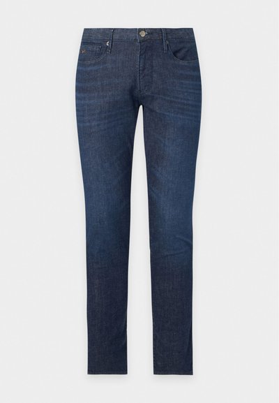 Σκούρο μπλε τζιν slim fit με μπροστινές τσέπες, θηλιές για ζώνη και κλείσιμο με κουμπί σε απλό λευκό φόντο.