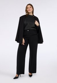 Czarne dopasowane spodnie o wysokim stanie, zestawione z błyszczącym czarnym swetrem i luźnym czarnym żakietem. Czarne buty na wysokim obcasie dopełniają look.