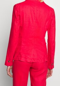 Red linen blazer with a tailored fit, featuring long sleeves, contrasting button hardware, and a smooth, textured finish.