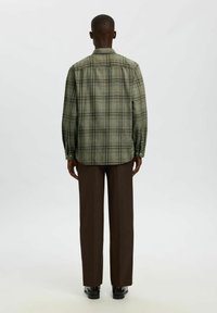 Zelena tartan flanelska srajca z dolgimi rokavi, gumbnimi manšetami, ovratnikom in ravnim robom, kombinirana s svetlo rjavimi hlačami ravnega kroja.