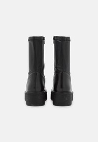 Bottes cheville en cuir noir à texture lisse, bout arrondi et fermeture éclair à l'arrière. Semelle en caoutchouc noire légèrement surélevée.