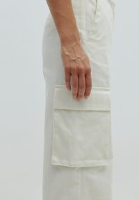 Witte cargo broek van textuurstof met een grote zijzak. Het ontwerp is recht toe recht aan, met subtiele verticale lijnen.