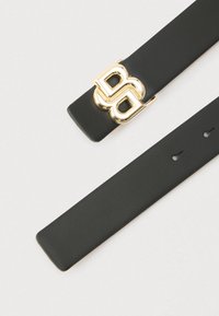 Čierny kožený opasok so zlatou prackou s prepleteným dizajnom písmena B. Hladká textúra s viacerými otvormi na nastavenie veľkosti.