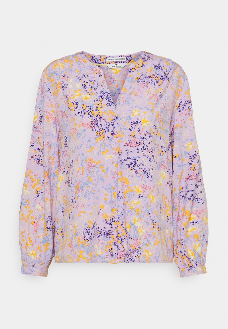 Blouse lavande claire avec col en V, manches longues et imprimé floral en jaune, orange et violet. Tissu doux et léger.