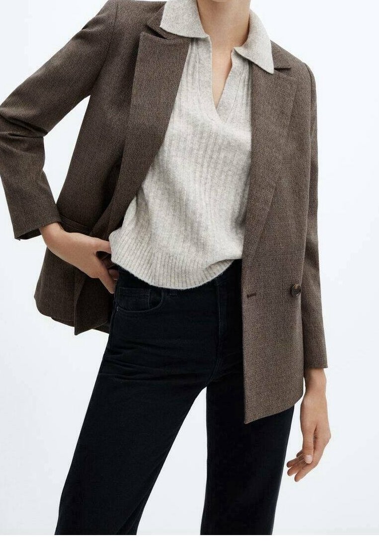 Hnědý strukturovaný blazer s klopami, kombinovaný se světle šedým žebrovaným svetrem a černými džíny. Blazer má detail na jednom knoflíku.