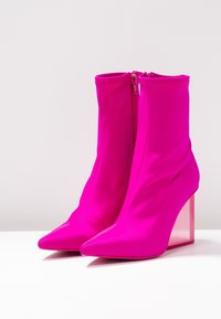 Bottines roses extensibles à talon, avec un bout pointu, featuring une fermeture éclair et un talon bloc translucide. Texture lisse et design épuré.