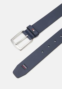 Cintura in pelle blu navy con fibbia quadrata in metallo argento. Presenta quattro fori per la regolazione e un piccolo logo in rosso e bianco. Tessuto liscio.