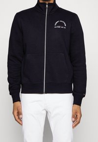 Felpa navy con zip, realizzata in un misto di cotone, con colletto alto, tasche frontali e design del logo bianco sul petto.