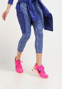 Sportowe legginsy w kolorze niebieskim z fakturowanym wzorem, w połączeniu z jasnoróżowymi butami biegowymi Nike z czarnymi akcentami.