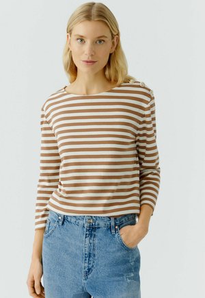 Bruin en crème gestreepte lange mouwen top met een bootnek en decoratieve knopen op de schouder, gecombineerd met lichte blauwe jeans.