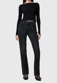 Haut noir côtelé à manches longues avec un col bateau, associé à un jean cargo droit avec poches latérales et une texture en denim noir délavé.