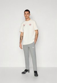 Kremfarget t-skjorte med liten rød og blå logo, kombinert med grå bomullssvetterbukser med hvit logo; svarte treningssko.